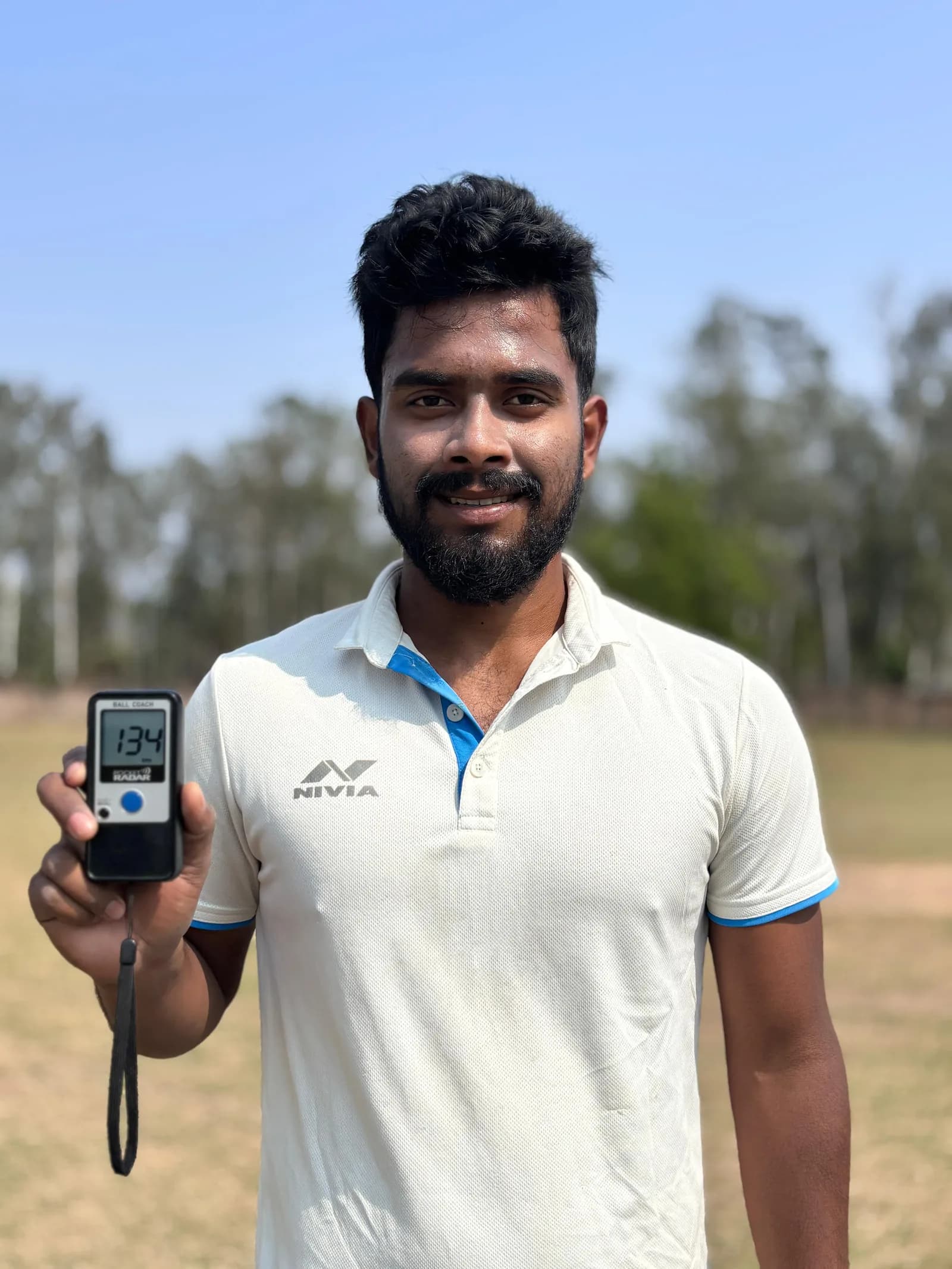 Fast bowling coach Ritom Borah holding a speed radar on a cricket ground